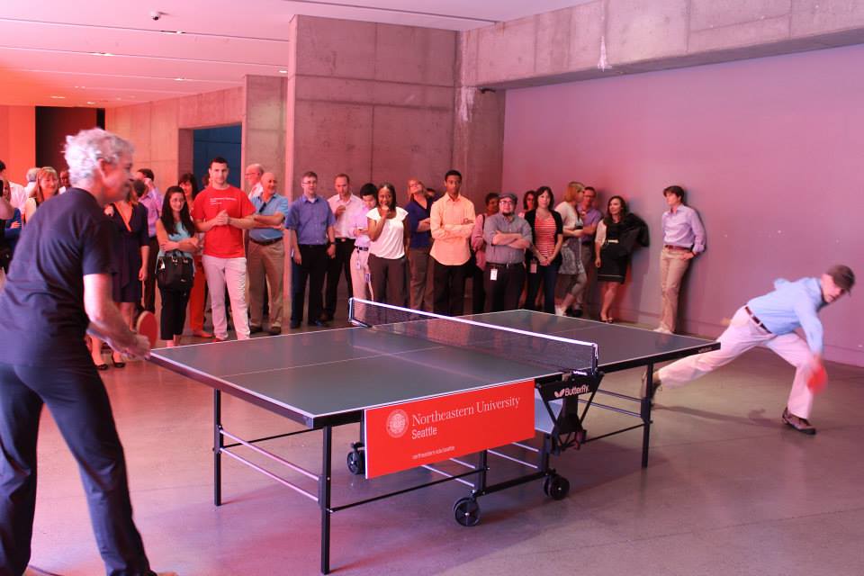 Two men playing a game of table tennis in front of a group of people.